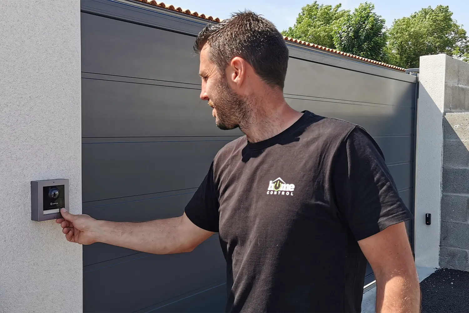 Technicien appuyant sur le bouton d'appel d'un visiophone connecté, installé sur un pilier à côté d'un portail